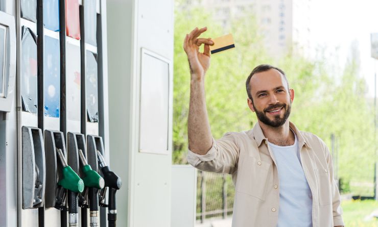 Ragazzo felice con la carta di credito nei pressi di un distributore di benzina