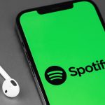 Spotify sullo sfondo di uno smartphone e con accanto delle cuffie