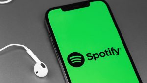 Spotify sullo sfondo di uno smartphone e con accanto delle cuffie